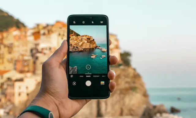Dłoń trzyma smartfon, na ekranie którego widać malowniczą włoską wioskę nad morzem. Chcesz wiedzieć, jak ulepszyć aparat w telefonie? Oto przykład pięknego ujęcia!