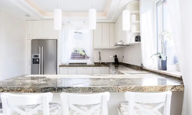 Plan de travail en granit, un danger potentiel pour les couteaux de cuisine. Cuisine moderne avec réfrigérateur, armoires blanches et tabourets.