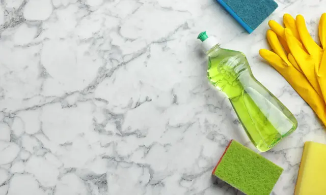 Reinigungsutensilien wie Spülmittel, Handschuhe und Schwämme liegen bereit, um Marmor zu reinigen.
