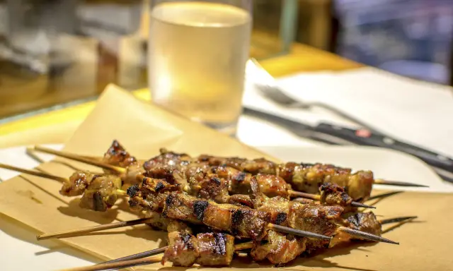Arrosticini, uno dei piatti tipici abruzzesi, serviti su carta paglia con un bicchiere di vino bianco sullo sfondo.