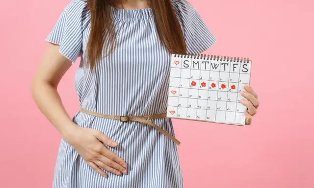 Kobieta z kalendarzem menstruacyjnym, który pokazuje dni okresu. Poznaj sposoby, jak zmniejszyć ból podczas okresu.