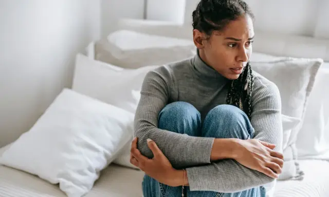 Donna seduta sul letto, abbracciata, con espressione preoccupata. Sembra soffrire di ansia da separazione dal partner.