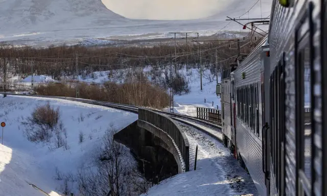 Tåg luleå narvik färdas genom ett snöigt landskap med berg i bakgrunden.