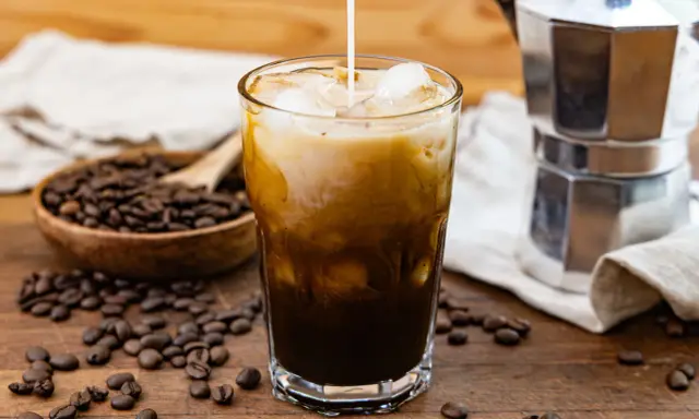 Ein Glas Eiskaffee mit Milch, Eiswürfeln und Kaffeebohnen. Perfekt für dein Cold Brew Rezept.