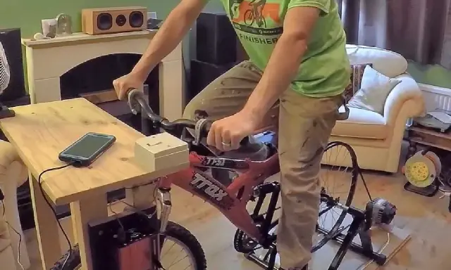 Un homme pédale sur un vélo d'appartement pour produire de l'électricité, chargeant son téléphone.