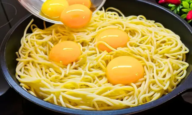 Makaron z jajkiem w patelni, żółtka tworzą złote kropki na żółtym tle.