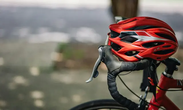 Czerwony kask rowerowy i kierownica z owijką. Niezbędne wyposażenie rowerzysty na bezpieczną podróż.