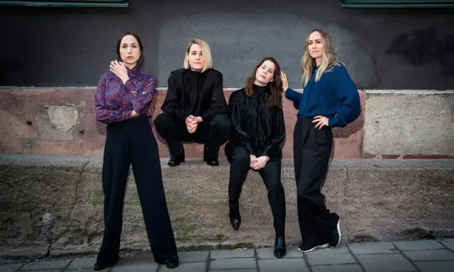 Sahara Hotnights medlemmar poserar framför en vägg. De bär mörka kläder och ser ut att vara redo för en fotografering.
