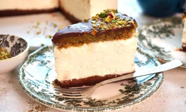 Sernik dubajski z polewą czekoladową i pistacjami, podany na ozdobnym talerzyku. Wygląda pysznie!