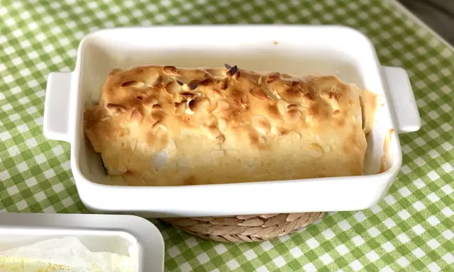 Bacalao gratinado con alioli, cubierto de almendras tostadas, en una fuente blanca sobre mantel de cuadros verdes.