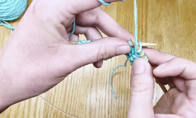 Manos tejiendo punto ojo de perdiz con hilo turquesa y agujas de madera.