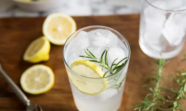 Orzeźwiający gin i tonic z plasterkiem cytryny i gałązką rozmarynu, otoczony świeżymi cytrynami.