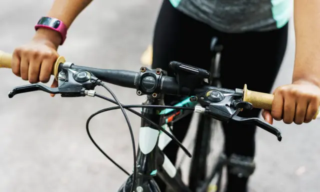 Ręce na kierownicy roweru, gotowe do jazdy. Widać manetki, hamulce i uchwyt na telefon. Trwa montaż licznika rowerowego.