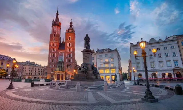 Rynek Główny w Krakowie o zachodzie słońca. Bazylika Mariacka i pomnik Mickiewicza. Ciekawe informacje o Krakowie znajdziesz w tym miejscu.