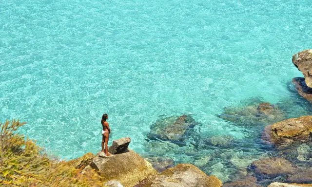Donna su scogli ammira acque cristalline, un gioiello delle aree marine protette in Italia.