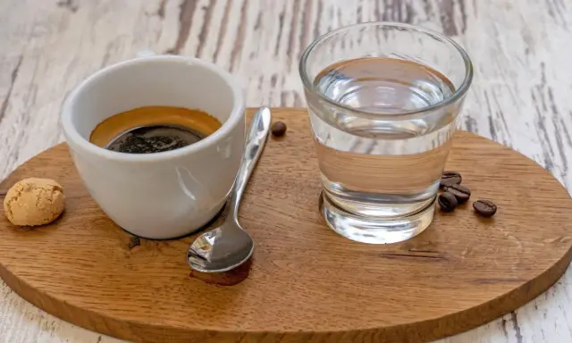 Espresso mit einem Glas Wasser, das die Aromen reinigt. Ein Keks und Kaffeebohnen vervollständigen das Bild.