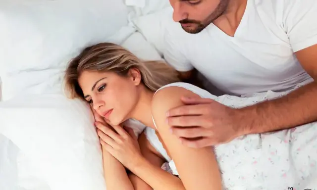 Mujer triste en la cama, su pareja la abraza. Ella piensa: "odio a mi pareja".