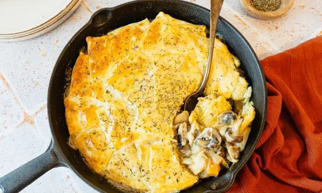 Une tourte aux champignons dorée et appétissante, servie dans une poêle en fonte, avec une cuillère prête à déguster.
