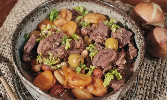 Un savoureux tajine de chevreuil mijoté avec des pommes de terre et des olives, garni de coriandre fraîche.