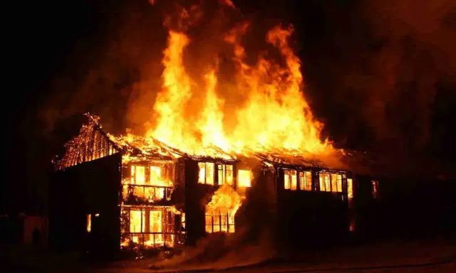 Une maison à deux étages est dévorée par les flammes, le toit s'effondre. L'incendie cause une destruction massive.