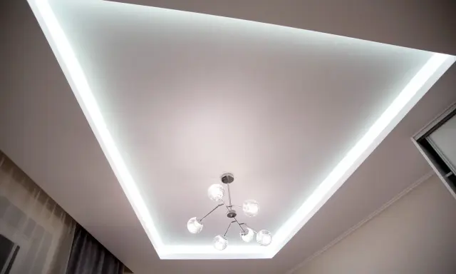 Nowoczesny sufit napinany lustrzany z podświetleniem LED i designerską lampą.