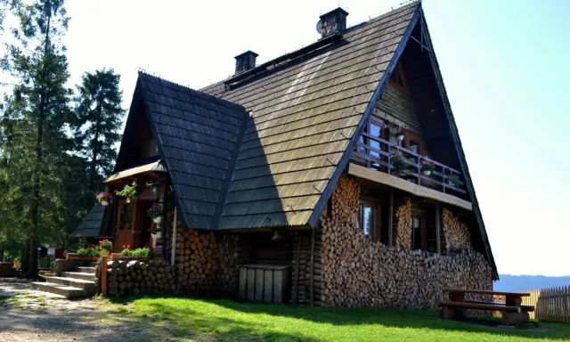 Drewniana bacówka na Turbaczu, z kamiennymi schodami i stosem drewna. Stare wierchy zapraszają do odpoczynku.