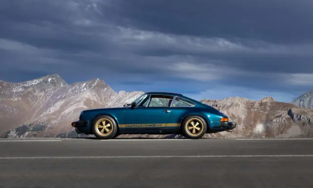 Ein türkisfarbener Porsche 911 SC mit goldenen Felgen und Streifen steht auf einer Bergstraße. Die Wertentwicklung dieses Klassikers ist beeindruckend.