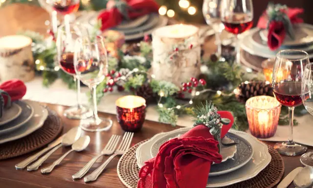 Tavola apparecchiata per un magico pranzo di Natale, con candele, pigne e luci scintillanti. Dove andare per un'atmosfera così?