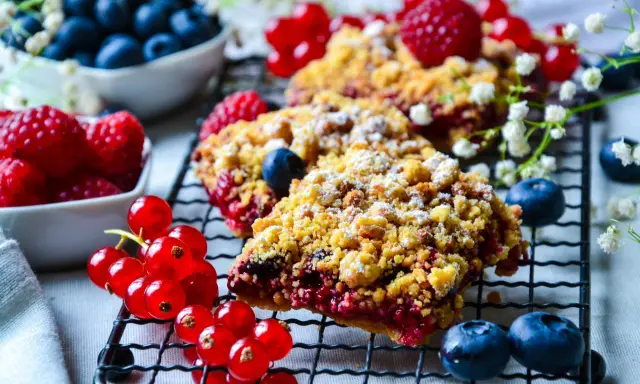 Délicieux crumble aux fruits rouges, garni de framboises, myrtilles et groseilles, saupoudré de sucre glace.