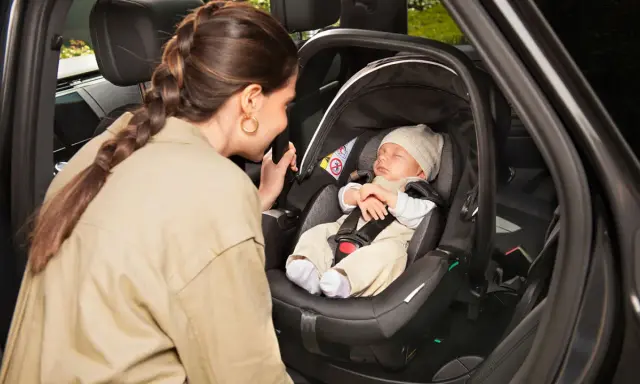 Madre mira a su bebé dormido en la silla coche, asegurando la correcta postura recien nacido silla coche para un viaje seguro.