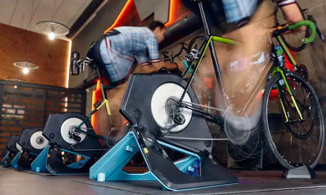 Intensywna jazda na rowerze w domu. Kilka rowerów stacjonarnych z trenażerami w akcji, tworząc wrażenie ruchu.