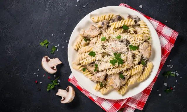 Pyszny makaron z kurczakiem i pieczarkami w kremowym sosie, posypany parmezanem i świeżą pietruszką.