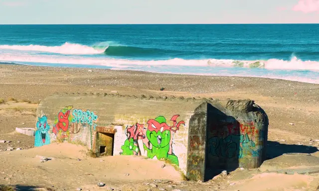 Bunker mit Graffiti am Strand von Klitmoller, Dänemark. Wellen brechen im Meer.