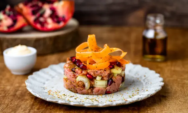 Deliziosa tartare di manzo con melograno, cipolla e carote a spirale, servita su un piatto rustico.