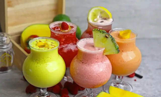 Cinq verres de boisson énergisante maison aux fruits colorés : jaune, rose, rouge et orange, garnie de fruits frais.