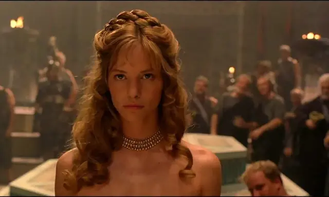 Die schöne Helena, Menelaos' Frau, blickt ernst in die Menge. Ihr Haar ist kunstvoll geflochten, ein goldenes Halsband schmückt ihren Hals.