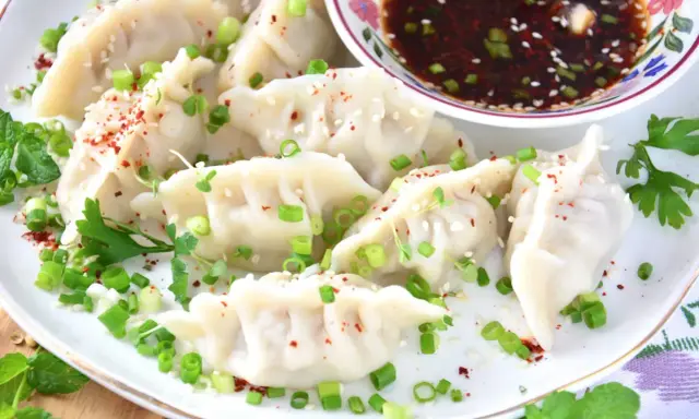 Pierożki gyoza, posypane szczypiorkiem i sezamem, podane z sosem.