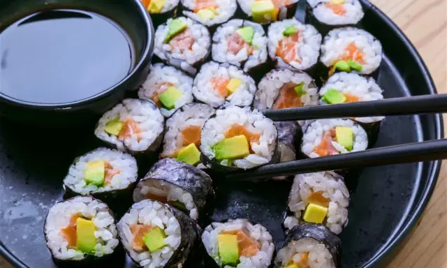 Un plato negro lleno de maki sushi de salmón y aguacate, listo para ser disfrutado con salsa de soja.