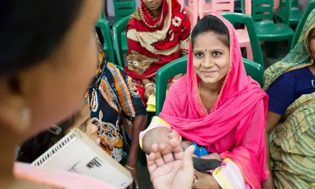 Frauen in bunten Saris, eine hält ein Baby. Sie sitzen auf Stühlen und hören zu. Wann ist sadaka ne zaman verilir?