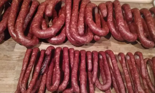 Dwie linie świeżej, swojskiej kiełbasy ułożone na drewnianym blacie. Idealne do wypróbowania przepisu na kiełbasę swojską.
