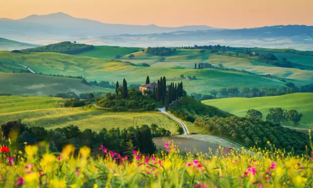 Un casale solitario su una collina, circondato da cipressi e dolci colline verdi, un sogno per un tour della Toscana.