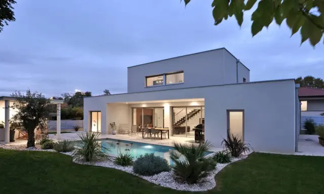 Vue arrière d'une maison moderne avec piscine illuminée, terrasse et jardin paysager. Un exemple de plan maison de luxe.