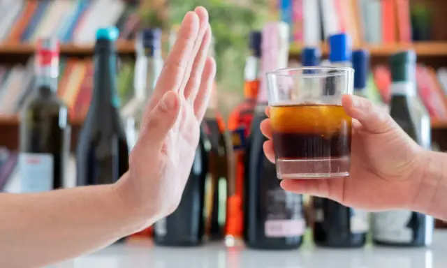 Dłoń odrzuca szklankę z alkoholem, symbolizując początek leczenia alkoholizmu.