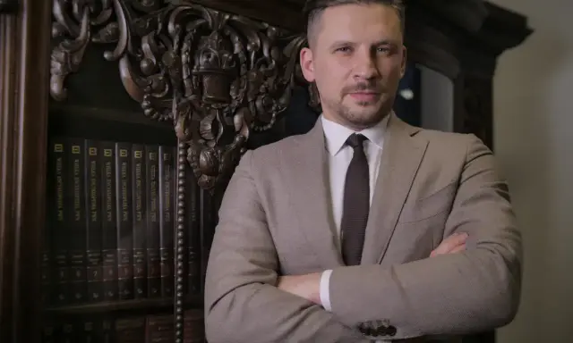 Mężczyzna w garniturze stoi na tle regału z książkami.