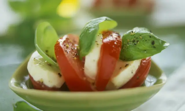 Tomate Mozzarella, ein gesundes Gericht, garniert mit frischem Basilikum und Pfeffer, serviert in einer grünen Schale.