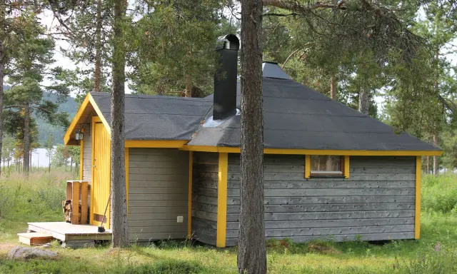 En mysig stuga för camping i Kiruna, omgiven av skog och med en sjö i bakgrunden.