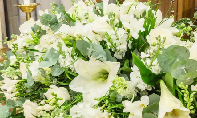 Piękna, biała wiązanka kwiatów z liliami, różami i zielonymi liśćmi.