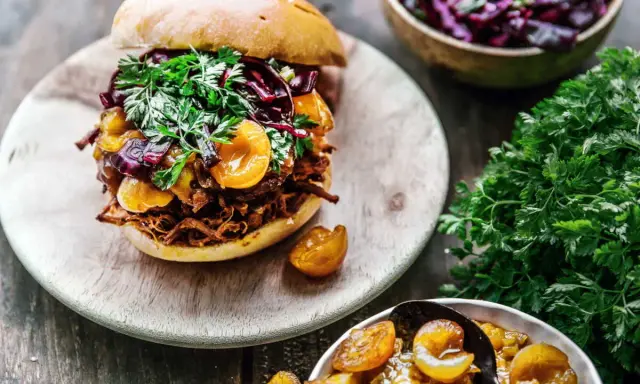 Un délicieux burger de pulled pork garni de fruits et de persil frais, accompagné d'une salade de chou rouge et de fruits confits.