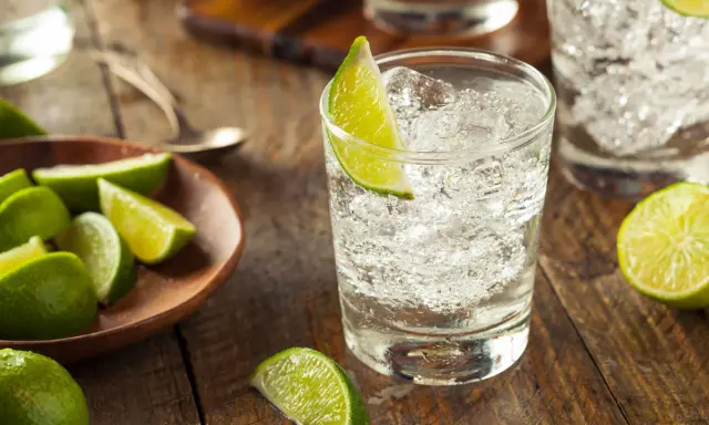 Erfrischender infused gin mit Eis und Limettenspalten auf rustikalem Holztisch.