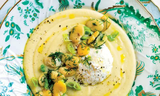 Macco di fave fresche cremoso, guarnito con fave intere, ricotta fresca e aneto, servito su un piatto decorato.
